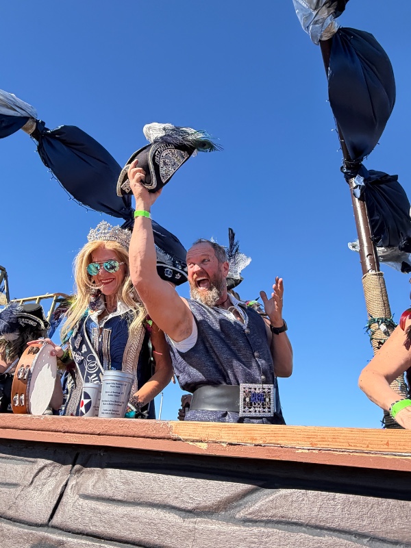 Man dressed as a pirate captain holding beads and interacting with a large crowd of people